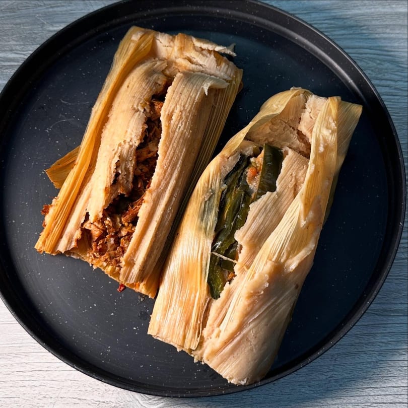Two tamales, one with shredded meat and the other with green chili, on a dark plate.