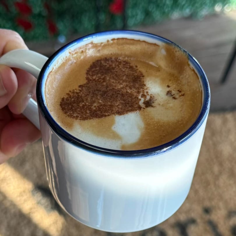Hand holding a white mug with a heart-shaped latte art on top of a frothy coffee.